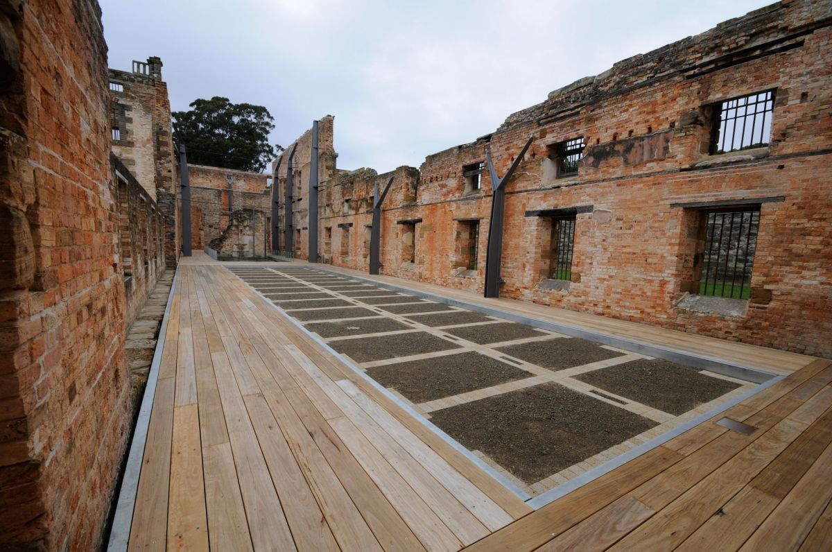 Ruins of a brick building with a wooden walkway and tiled floor under an open sky