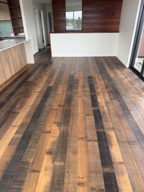 Empty modern room with wood-look plank flooring, light walls, and kitchen cabinets on the left.