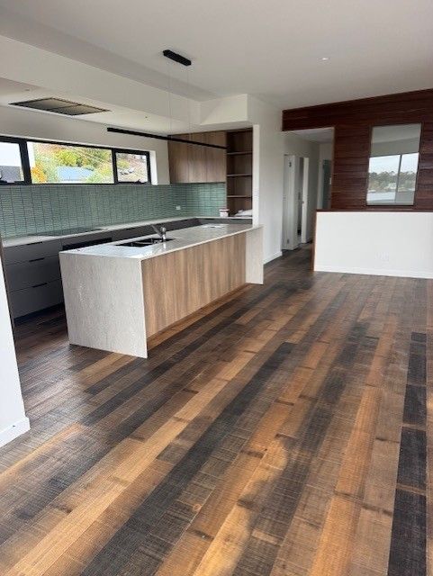 Modern open-plan kitchen with wood flooring, island, and white walls.