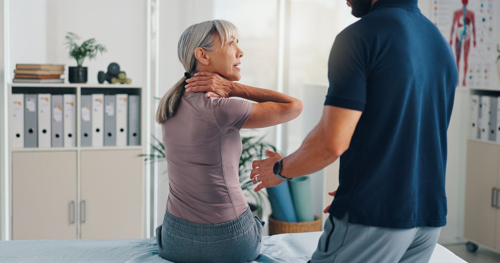 Physical therapist assisting seated patient with shoulder exercise in a clinic room