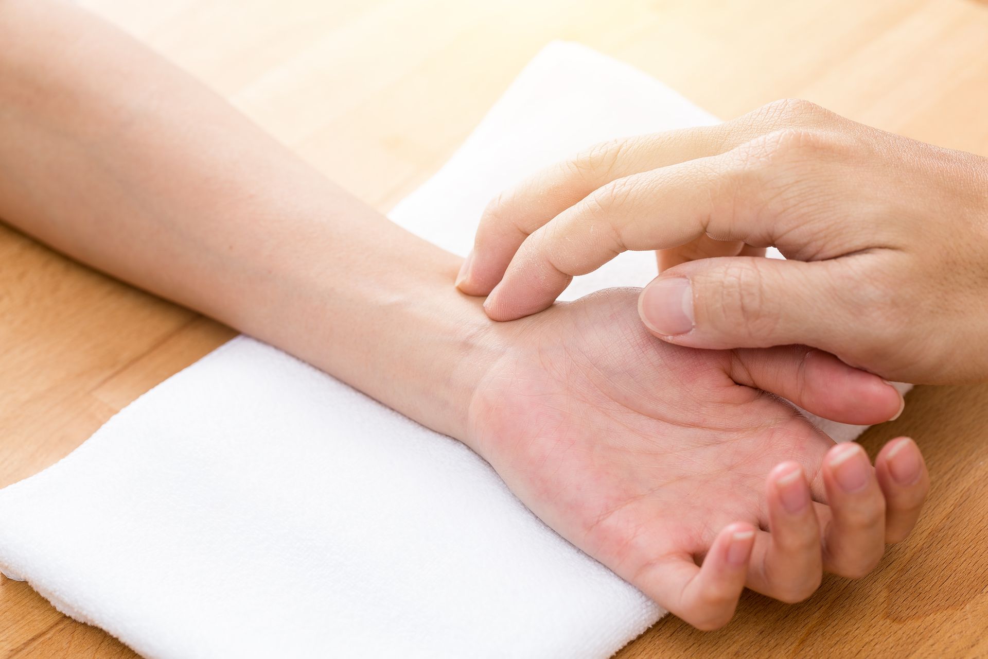 Hand gently holding a wrist on a white towel over a wooden table