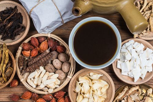 Assorted herbs and nuts around a cup of dark tea on a wooden table