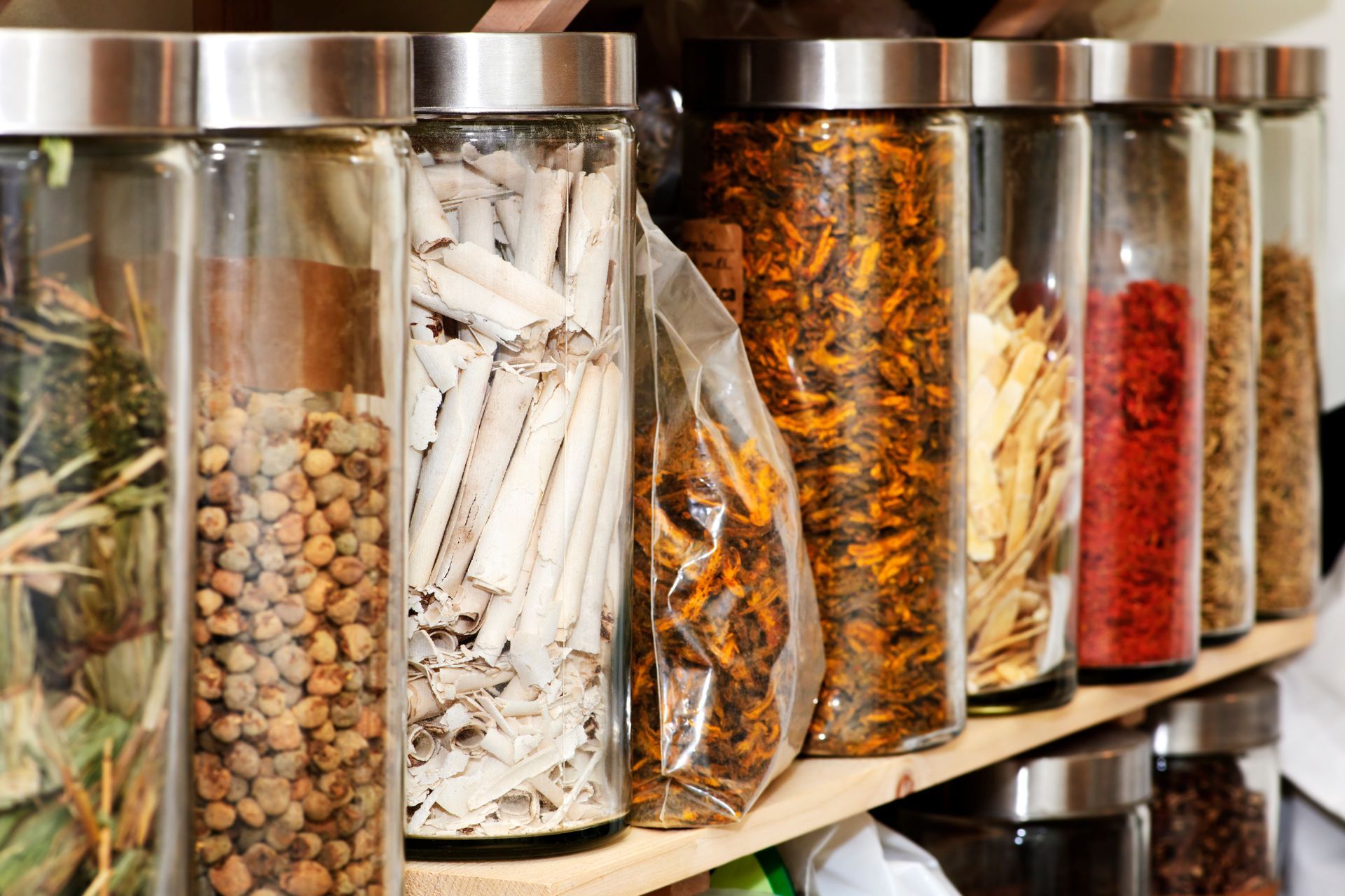 Glass jars of assorted dried spices and herbs lined up on a kitchen shelf.