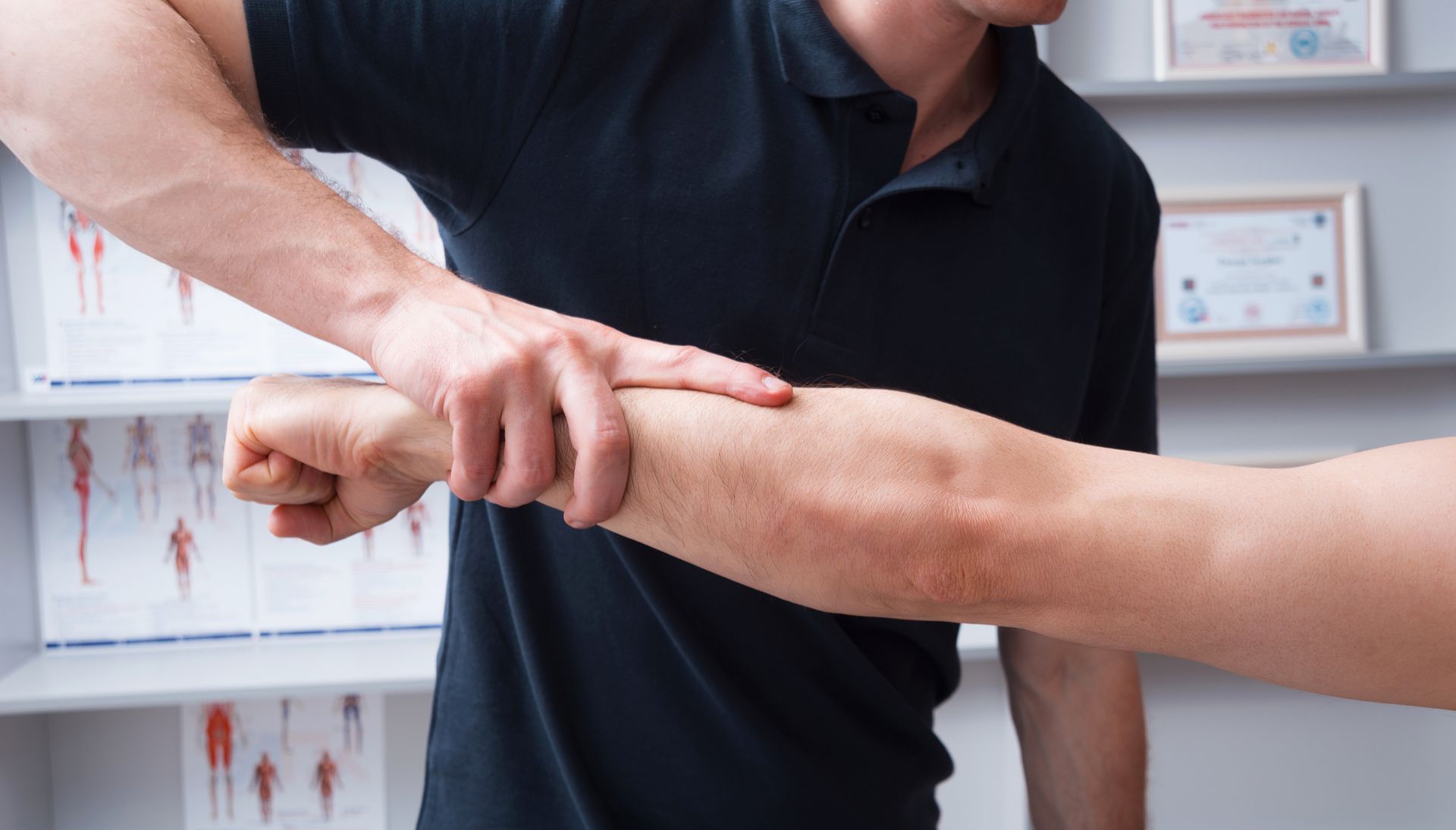 Therapist stretching a patient’s arm in a clinic, with medical charts in the background