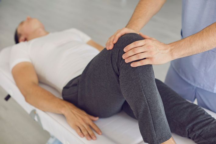 Physical therapist bending a patient’s knee during a leg exercise on a treatment table