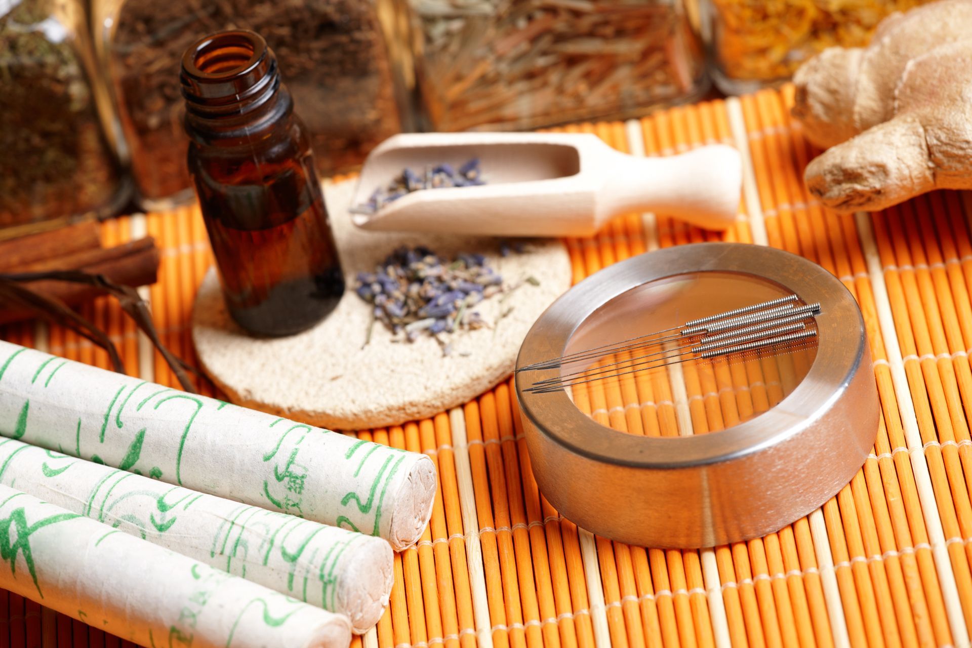 Herbal spa setup with rolled towels, amber bottle, white scoop, and bowl on a bamboo mat