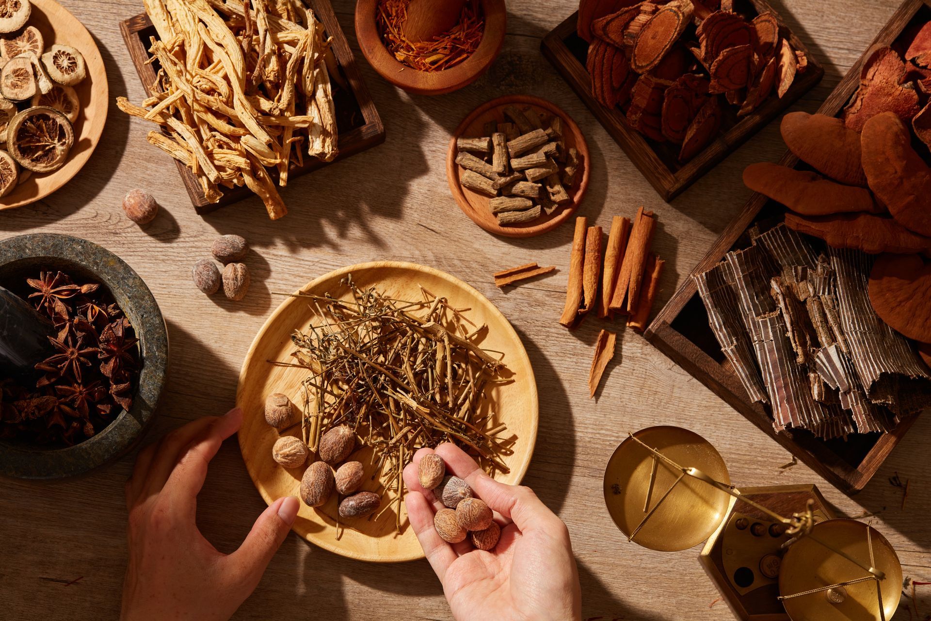 Hands arranging spices on a plate beside assorted spices, cinnamon sticks, and a glass of tea on a warm tabletop