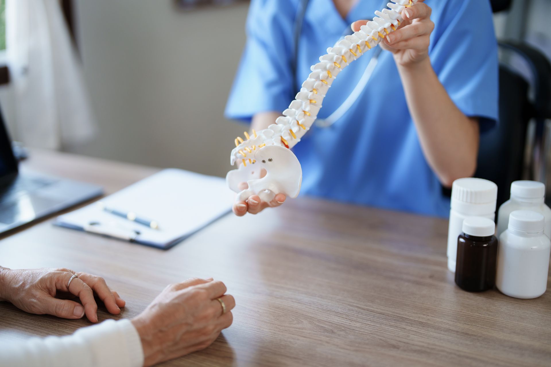 Doctor showing spine model to patient at a desk with bottles and paperwork