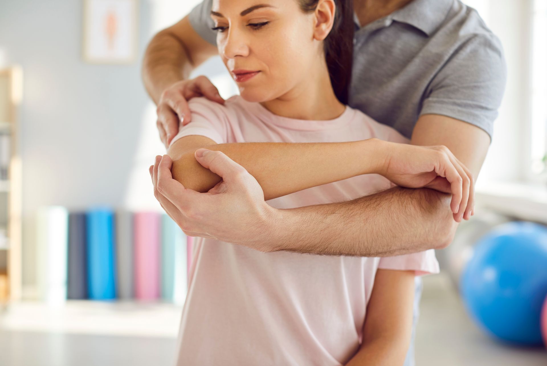 Person receiving a shoulder massage in a bright room, with a therapist standing behind them