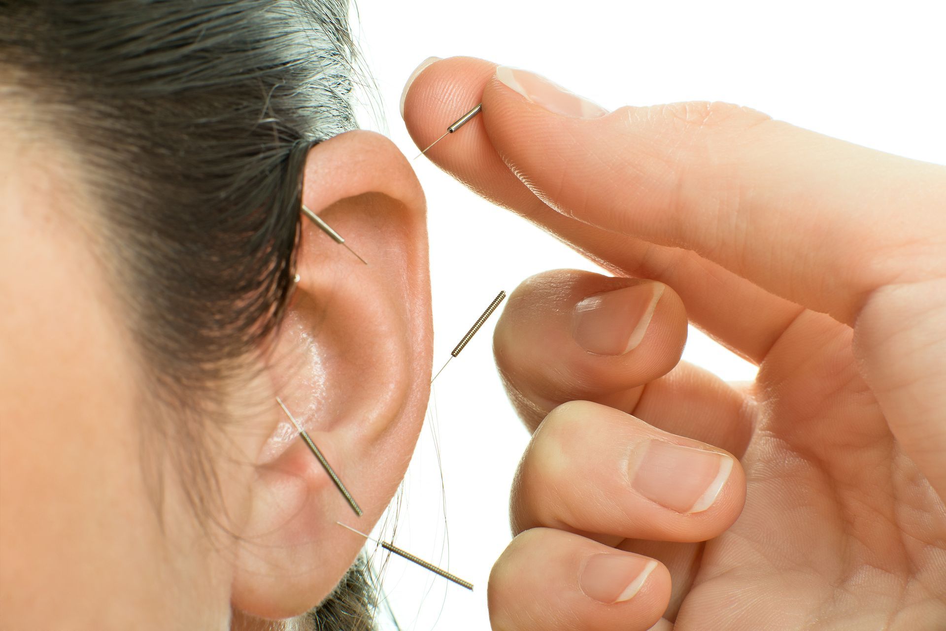 Hands adjusting a green ear loop on a person's ear against a white background