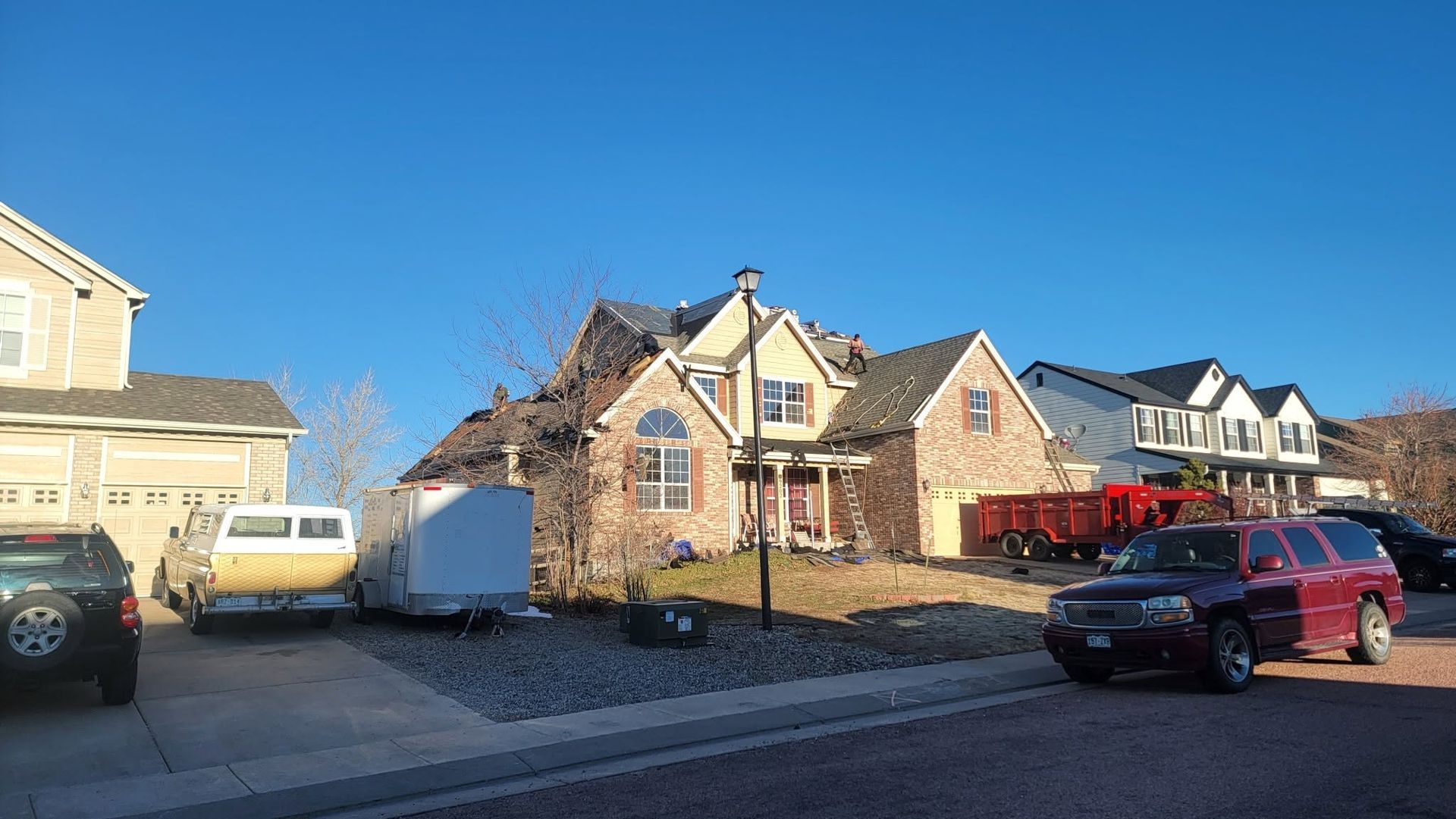 Suburban street with parked cars and brick houses under a clear blue sky