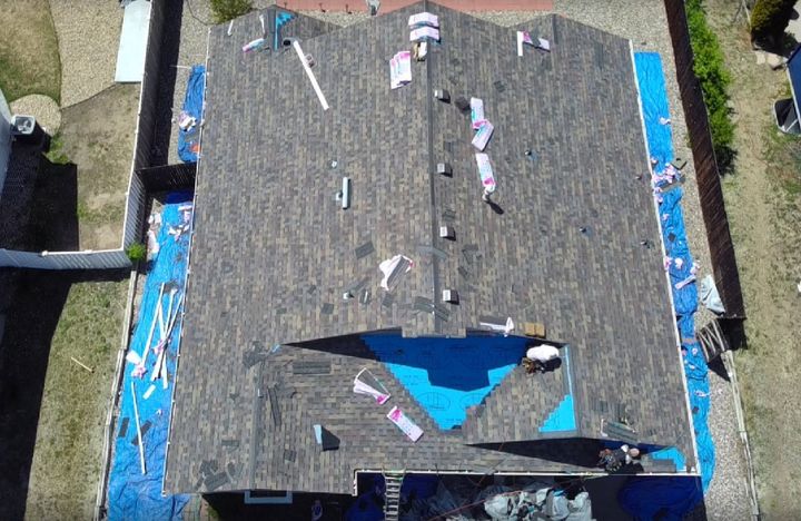 Aerial view of a house roof with visible damage and a large blue tarp covering part of it
