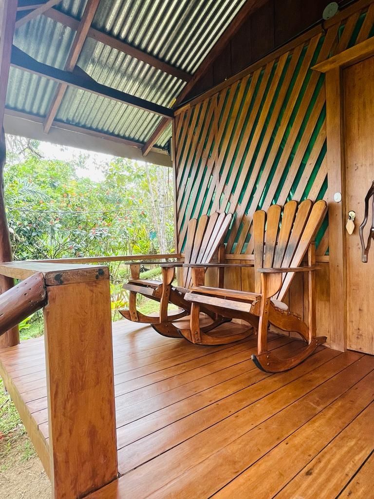 Wooden porch with rocking chairs under a corrugated metal roof, overlooking greenery.