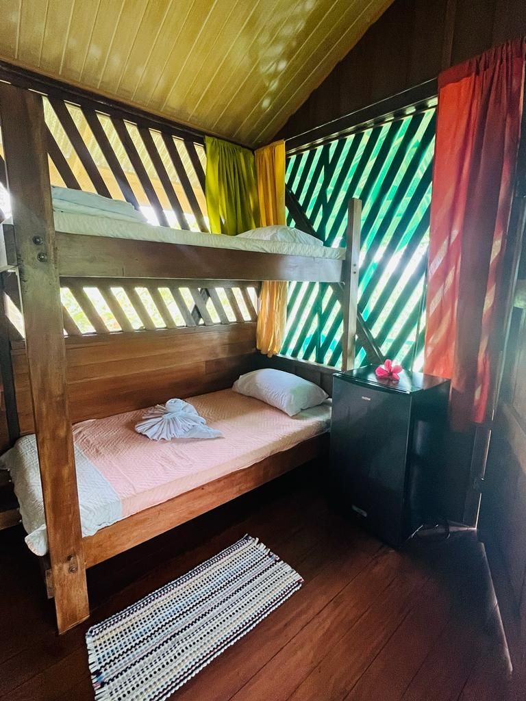 Bunk beds in a small room with slatted walls, a small fridge, and colorful curtains.