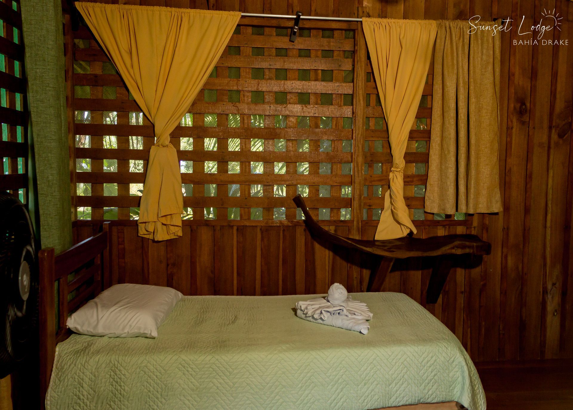 Wooden room with a bed, yellow curtains, and a decorative wooden wall, providing natural light.