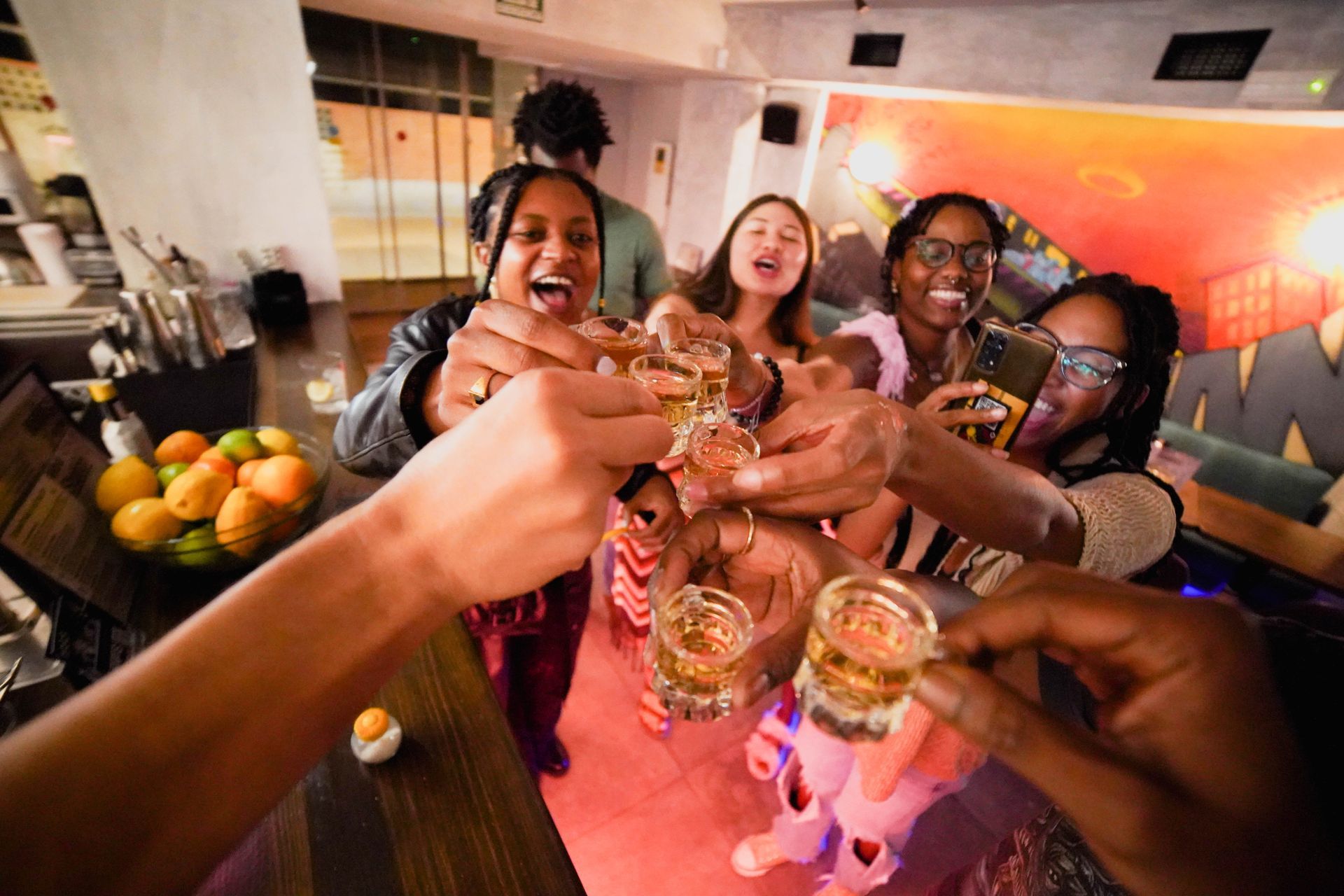 A group of people are toasting with shot glasses in a bar.
