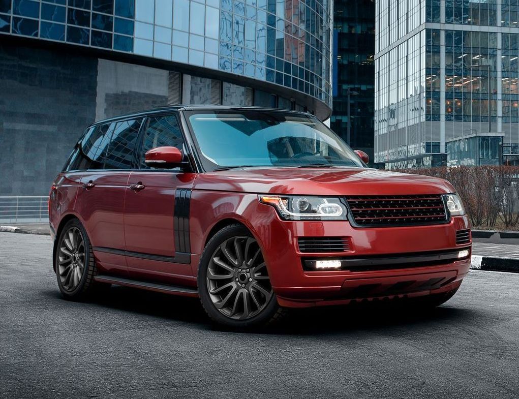 Red Range Rover parked on a city street in front of a modern glass skyscraper.