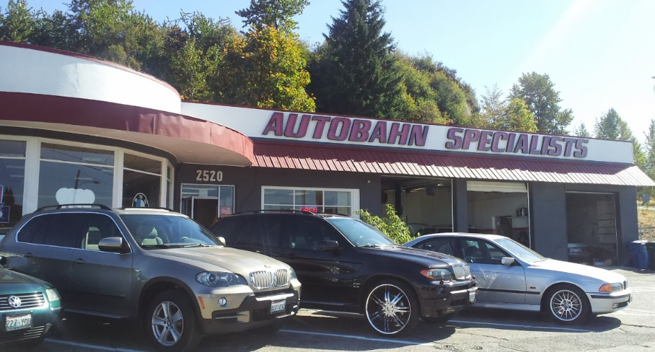 A grey, a black, and a silver car parked in front of an automotive repair shop named 
