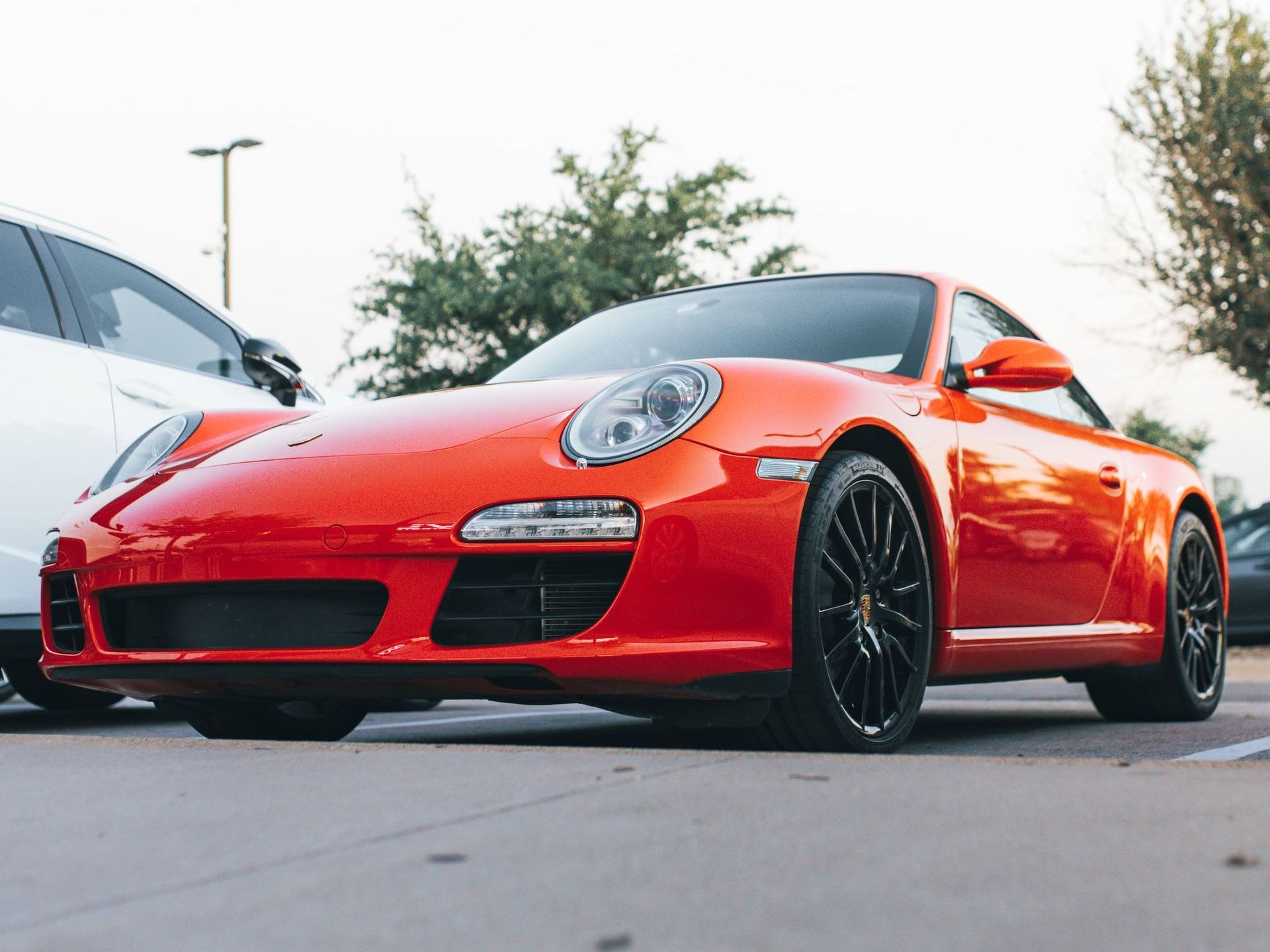 A low-angle, close-up shot of a bright orange Porsche sports car parked in an outdoor lot.