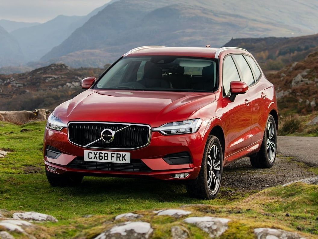 A bright red Volvo SUV parked on a grassy, mountainous landscape.