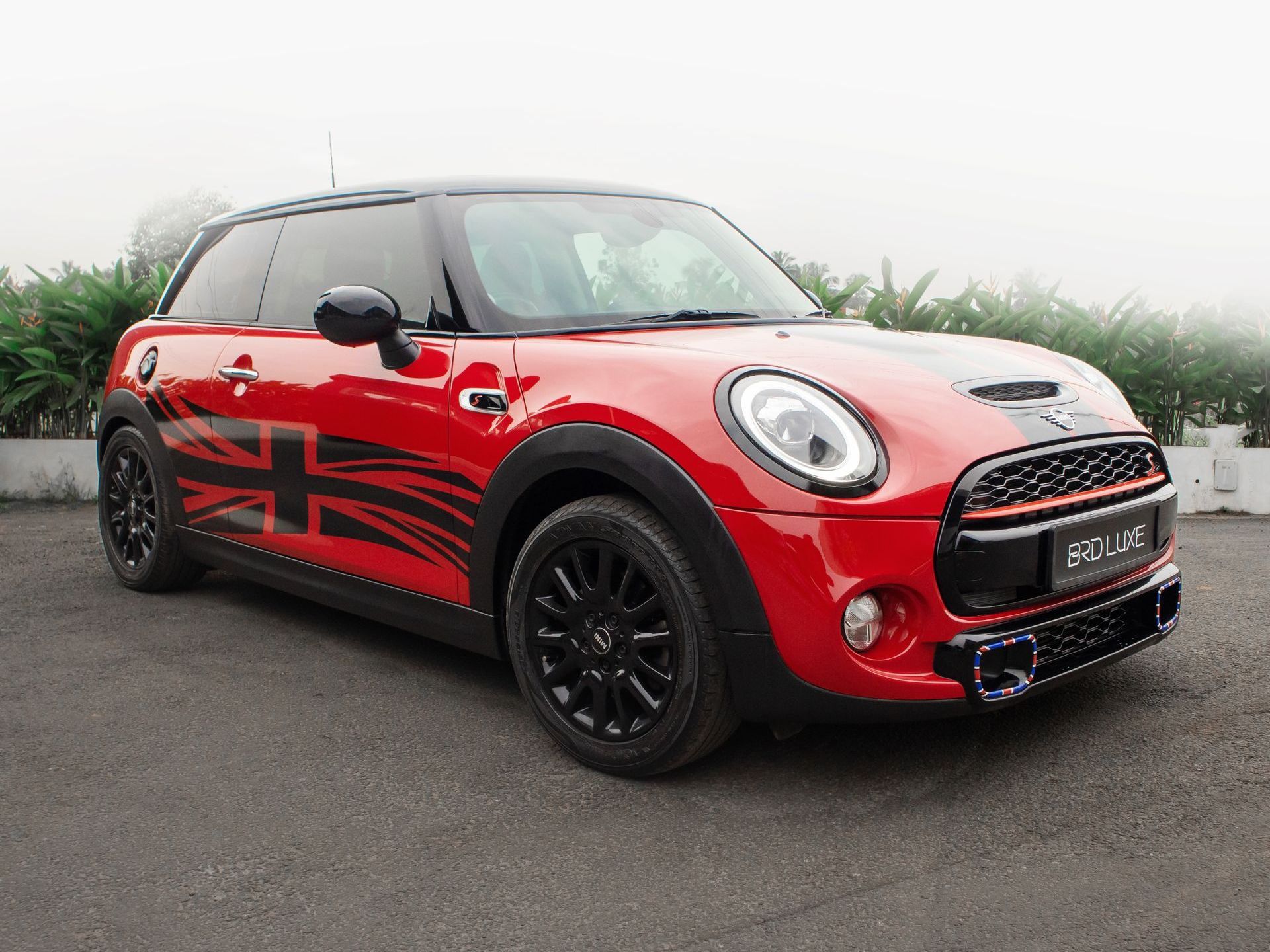A red MINI Cooper hatchback with a black roof and Union Jack side decals parked on a gravel surface.