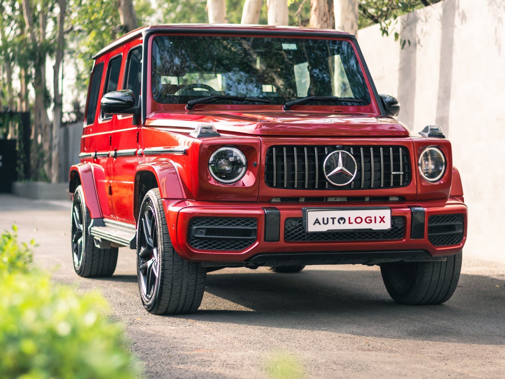 A bright red Mercedes-Benz G-Wagon parked on a tree-lined driveway during the day.