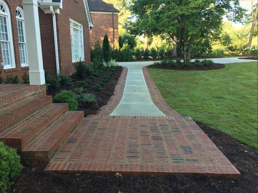 A brick walkway leading to the front of a brick house.