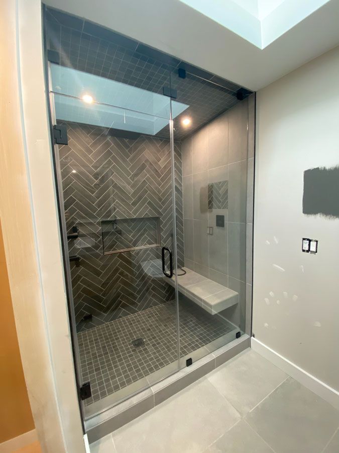 Modern bathroom with glass walk-in shower, herringbone tile, built-in bench, and light gray walls