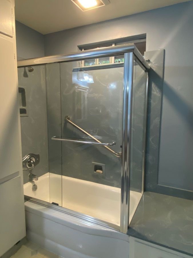 Accessible glass shower stall with a metal grab bar in a blue-gray bathroom