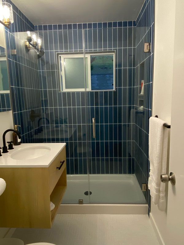 Blue-tiled bathroom with a sink, mirror, toilet, and glass-enclosed shower/tub.