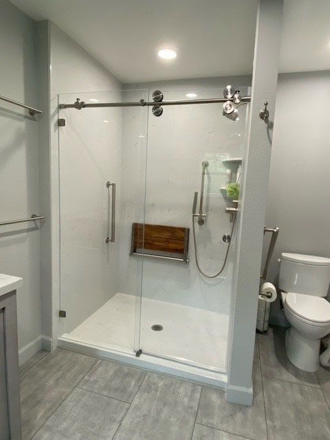 Modern bathroom with glass walk-in shower, gray tile floor, and toilet on the right.