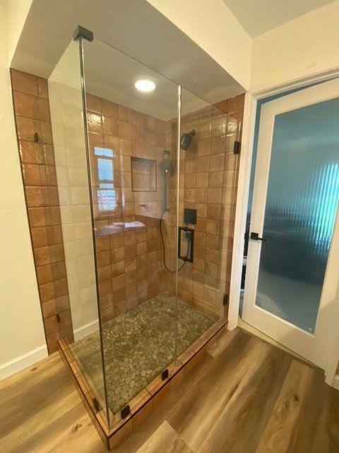Glass shower enclosure with tan tile walls and pebble floor in a bathroom