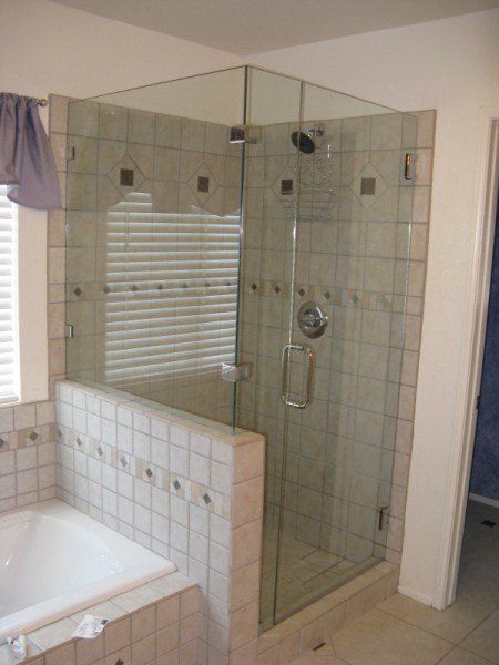 Bathroom with glass corner shower enclosure beside a tiled bathtub.