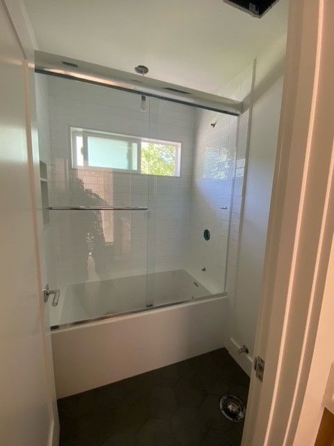 Modern bathroom with a white bathtub, glass shower screen, and frosted window.
