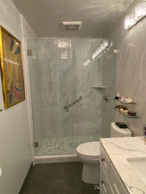Small bathroom with a glass-enclosed shower, toilet, sink, and marble countertop.