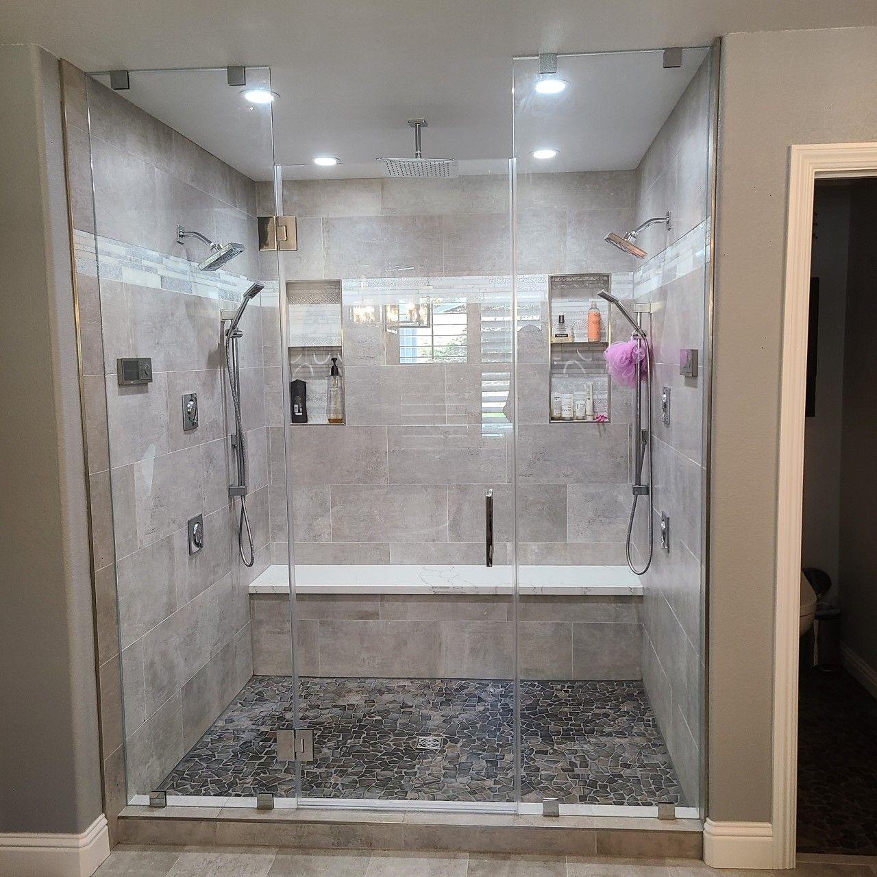 Modern glass walk-in shower with bench, gray tile, and multiple showerheads