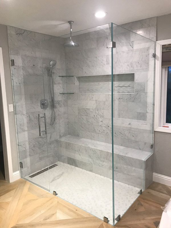 Glass-enclosed walk-in shower with gray tile, built-in bench, and chrome fixtures in a modern bathroom