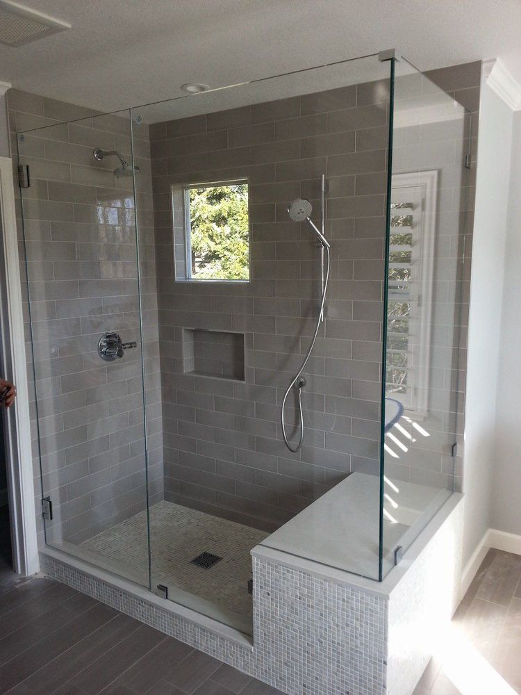 Glass walk-in shower with tiled bench, rain showerhead, handheld wand, and small window inside bathroom