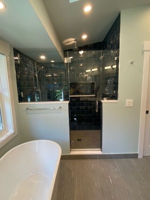 Modern bathroom with a white tub, gray floor, and a dark tiled walk-in shower.
