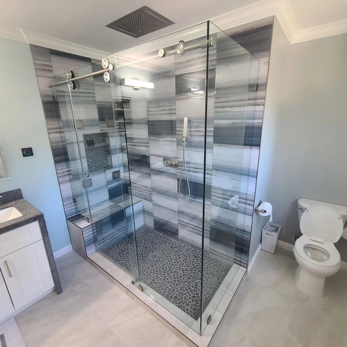 Modern bathroom with a glass walk-in shower, patterned tile walls, and a toilet beside it