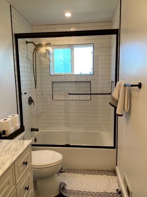 Bathroom with glass-enclosed shower, toilet, vanity, and towel bar next to a tiled wall.