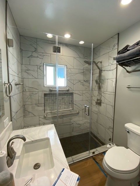 Compact tiled bathroom with walk-in glass shower, sink, and toilet.