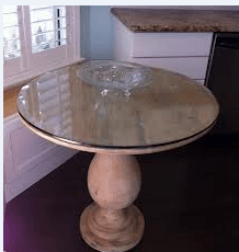 Round glass-top table with beige pedestal base beside a window in a bright room