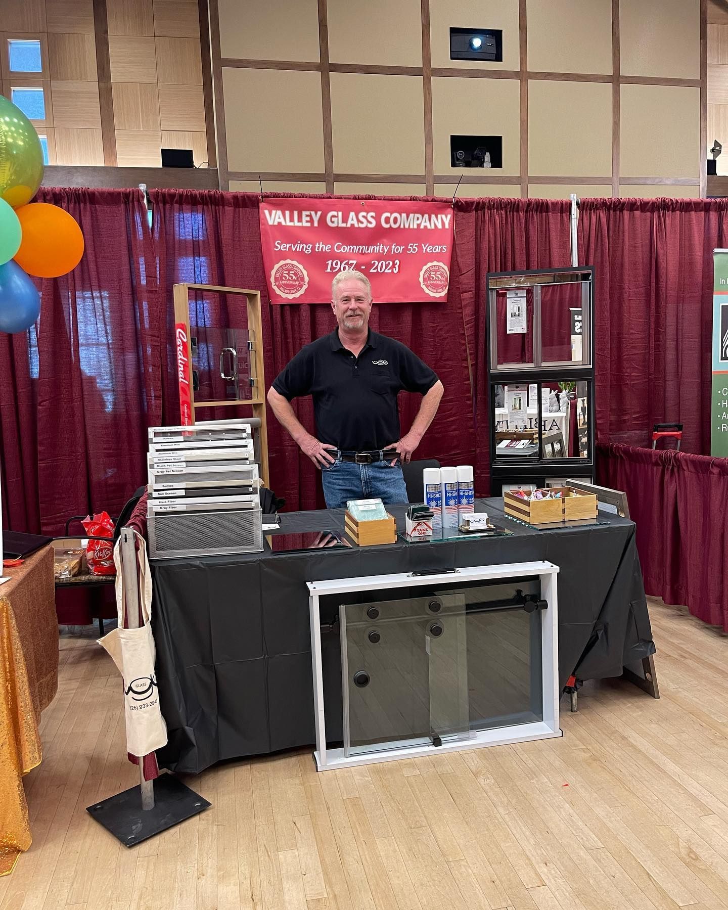 Man behind a booth with glass samples and tools at a trade show, red banner reading Valley Glass Company