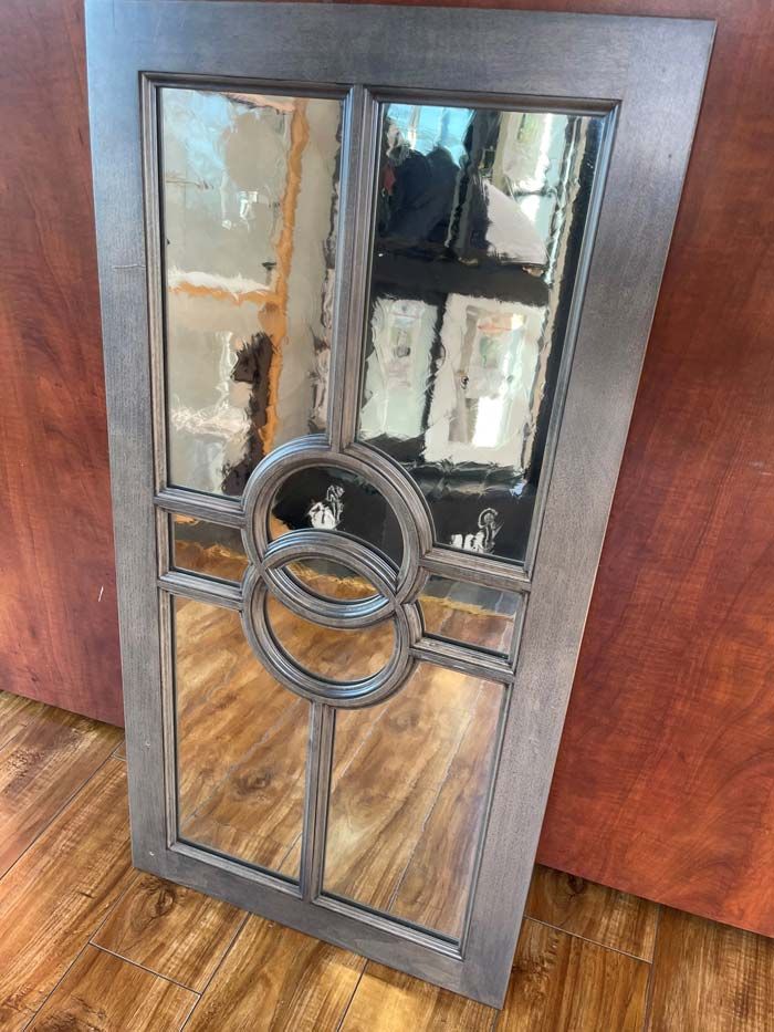 Decorative dark wood-framed mirror with circular metal accent, leaning against a wall on a hardwood floor