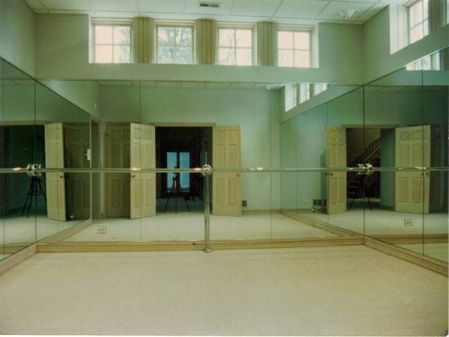 Empty mirrored room with high windows, pale walls, and wooden doors