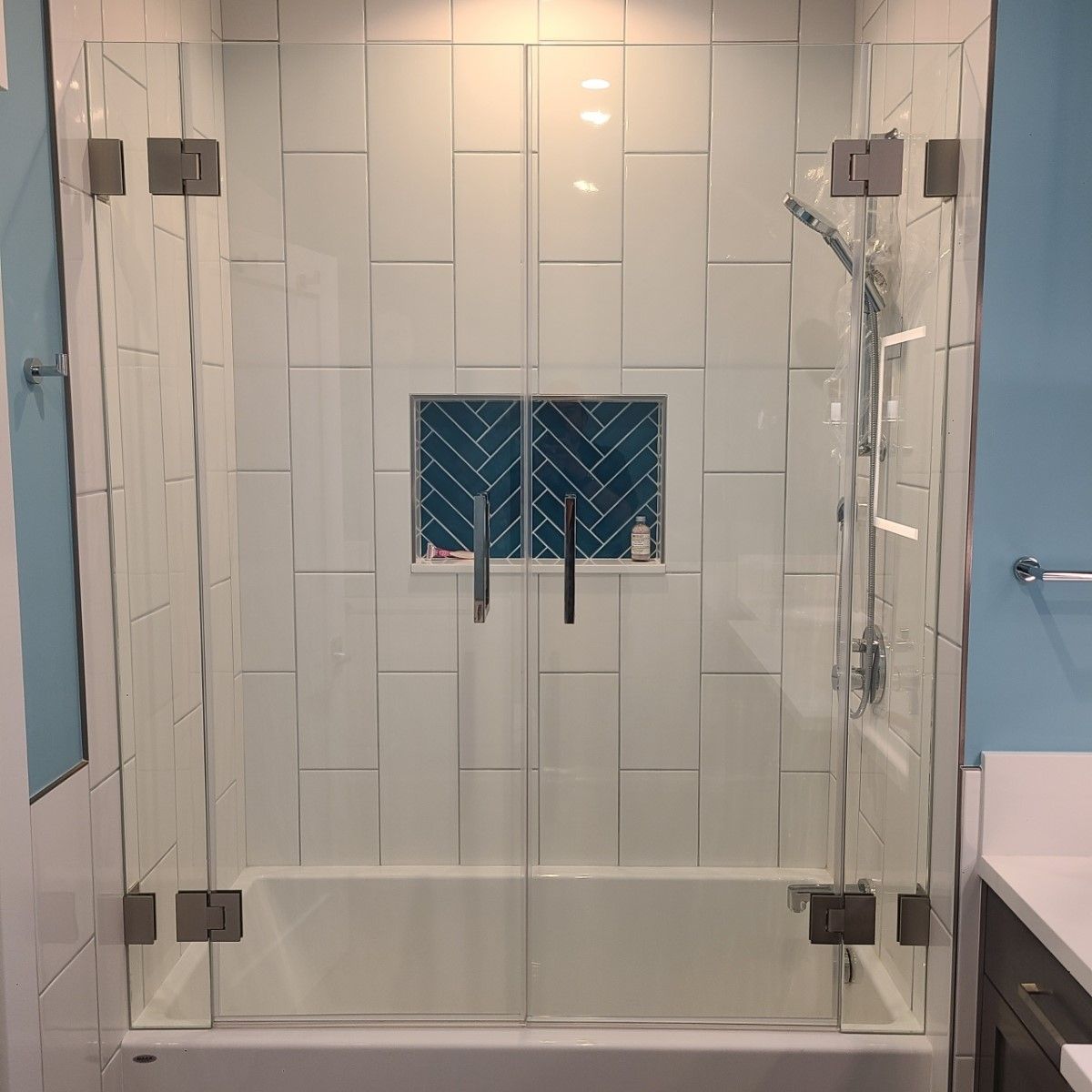 Glass shower enclosure with white subway tile, blue accent niche, and chrome fixtures