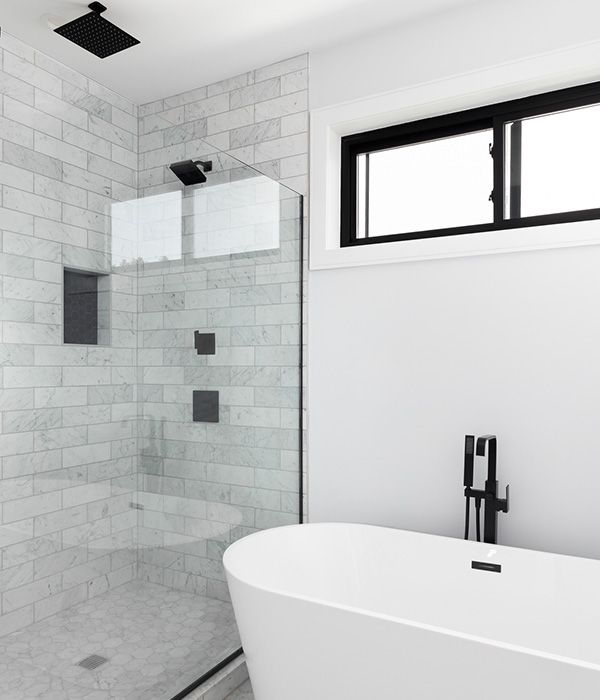 Modern bathroom with glass shower, white tile, black fixtures, and a freestanding tub