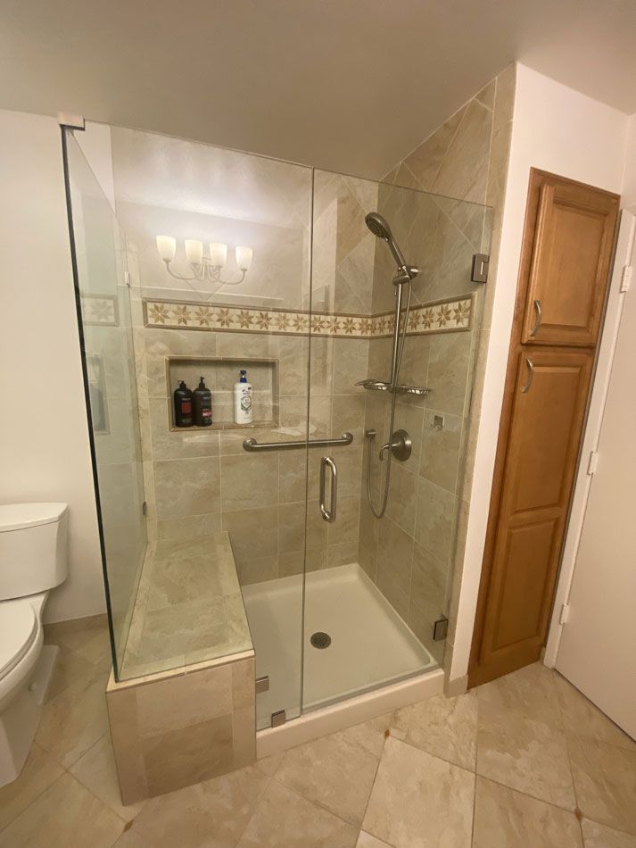 Bathroom with glass walk-in shower, beige tile, built-in shelf, and toilet beside it.