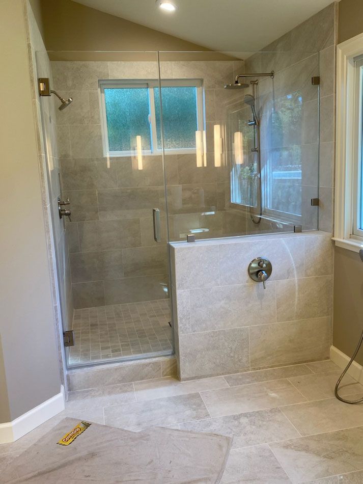 Modern tiled bathroom with a glass walk-in shower, bathtub, and frosted window.